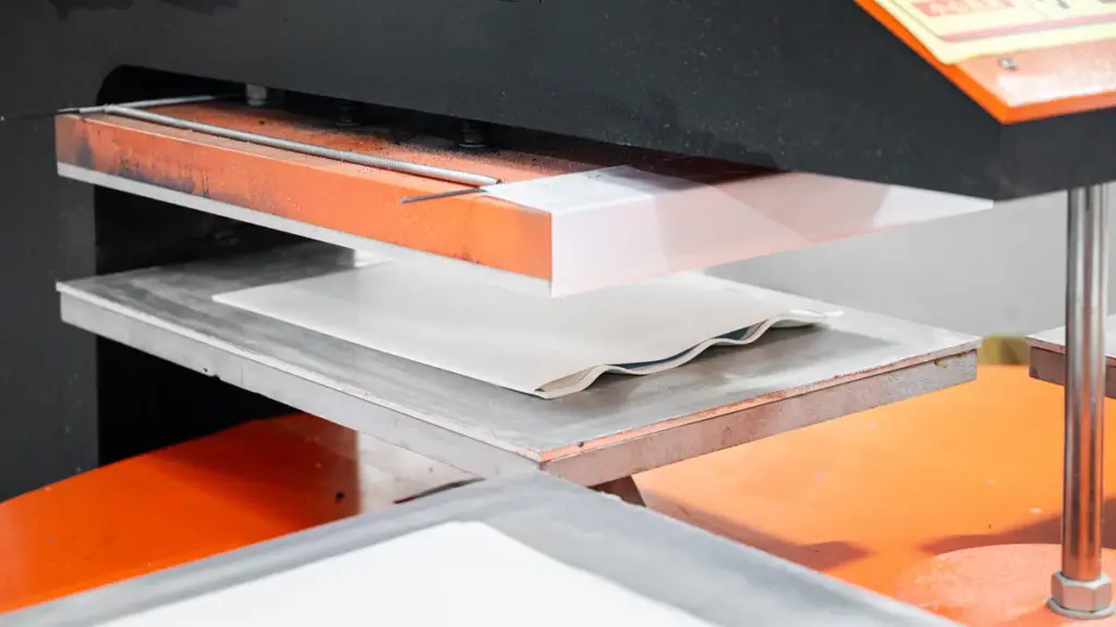 Close-up of industrial heat press machine processing white sheet material