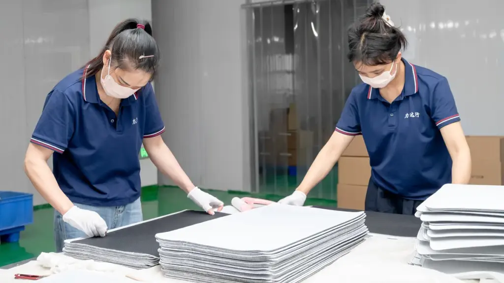 Two female workers in face masks inspecting stacked mouse pads