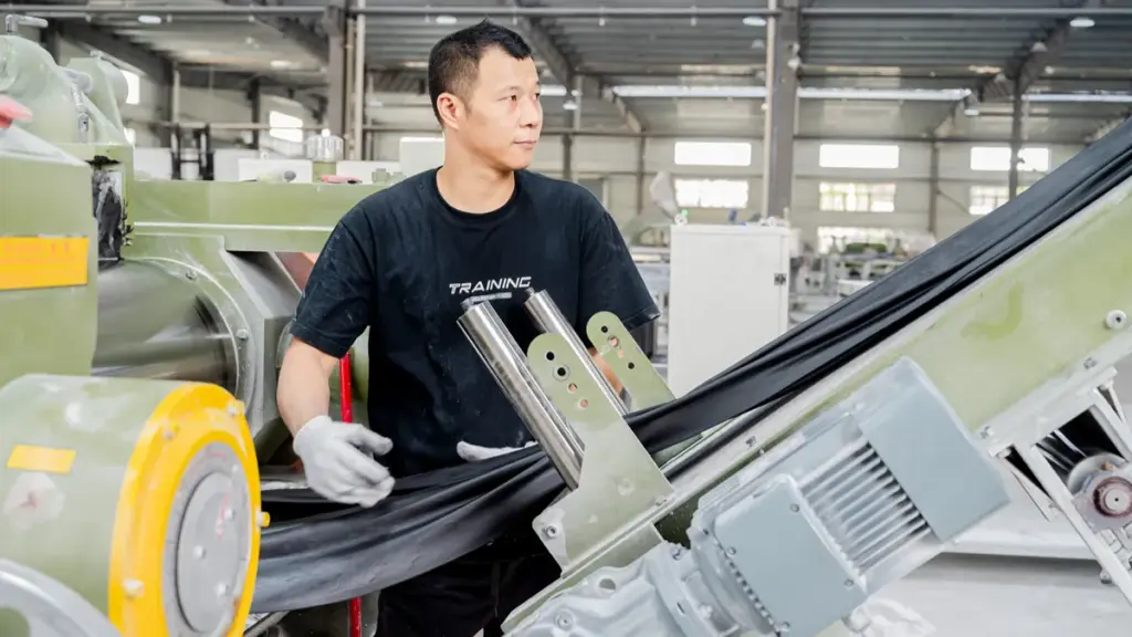 Worker processing black rubber sheet material on industrial factory machinery